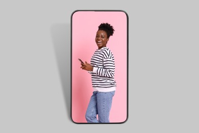 Image of Happy woman with smartphone on screen of big mobile phone on grey background