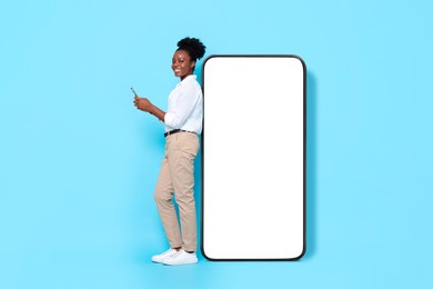 Image of Happy woman with smartphone leaning on big mobile phone with blank screen on light blue background