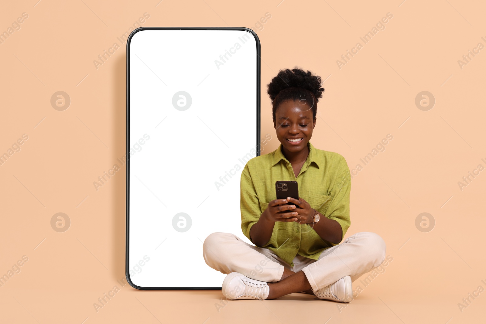 Image of Happy woman with smartphone sitting on beige background. Big mobile phone with blank screen behind her