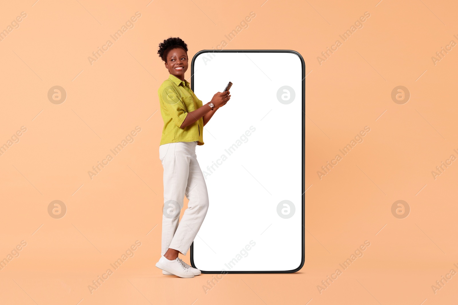 Image of Happy woman with smartphone on beige background. Big mobile phone with blank screen behind her