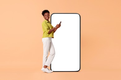 Image of Happy woman with smartphone on beige background. Big mobile phone with blank screen behind her