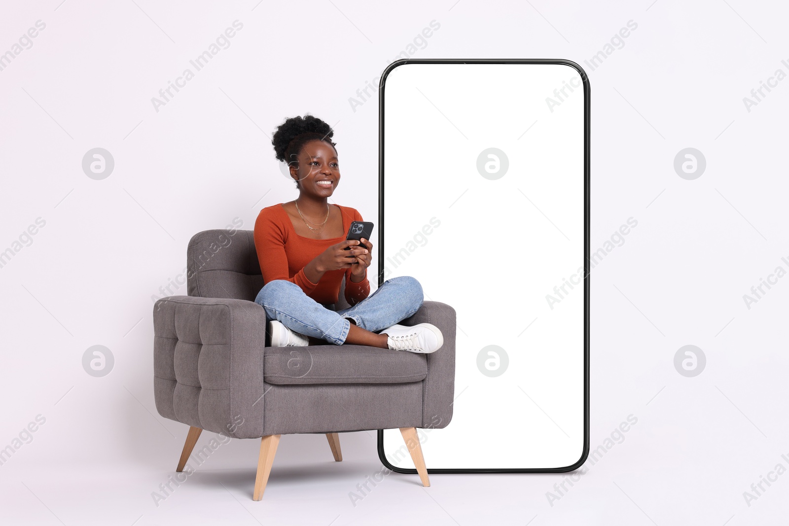 Image of Happy woman with mobile phone sitting in armchair on white background. Big cell phone with blank screen near her