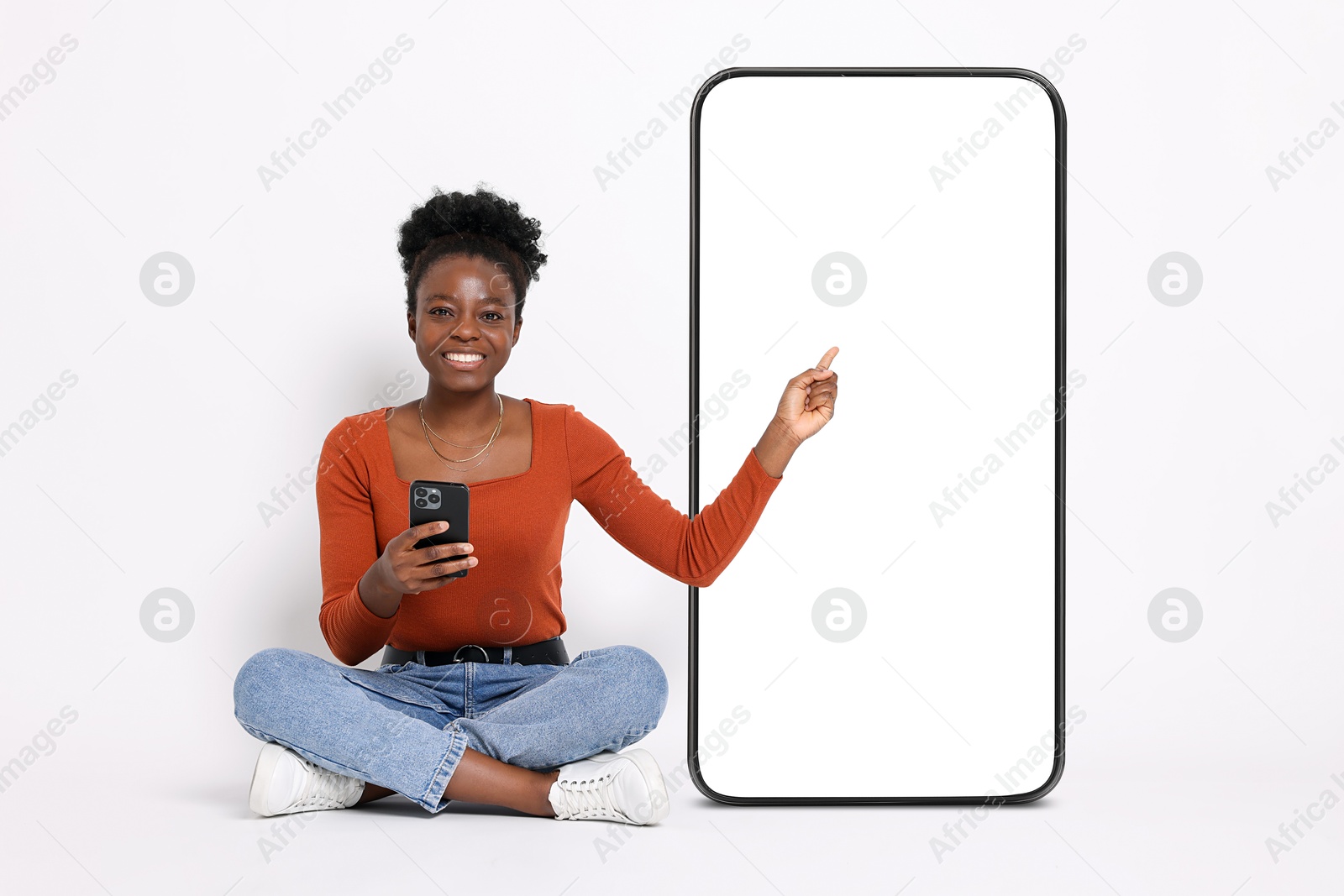 Image of Happy woman with smartphone pointing at big mobile phone with blank screen on white background