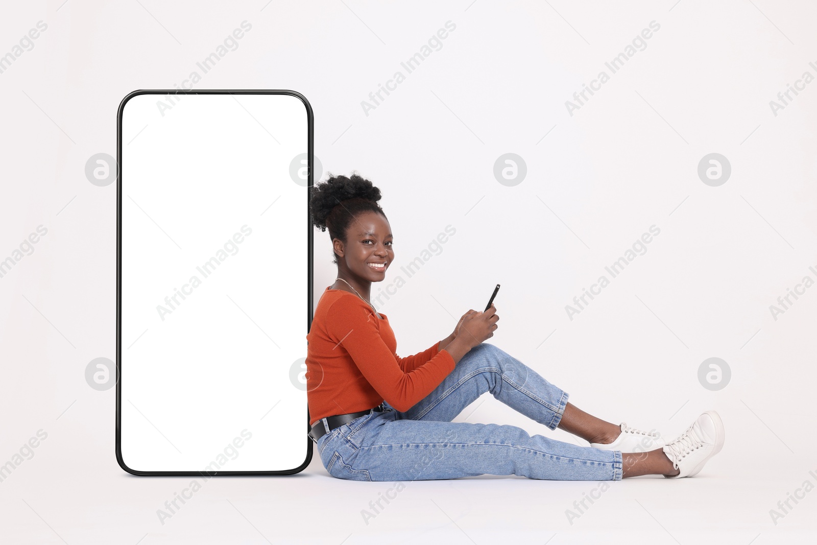 Image of Happy woman with smartphone leaning on big mobile phone with blank screen on white background