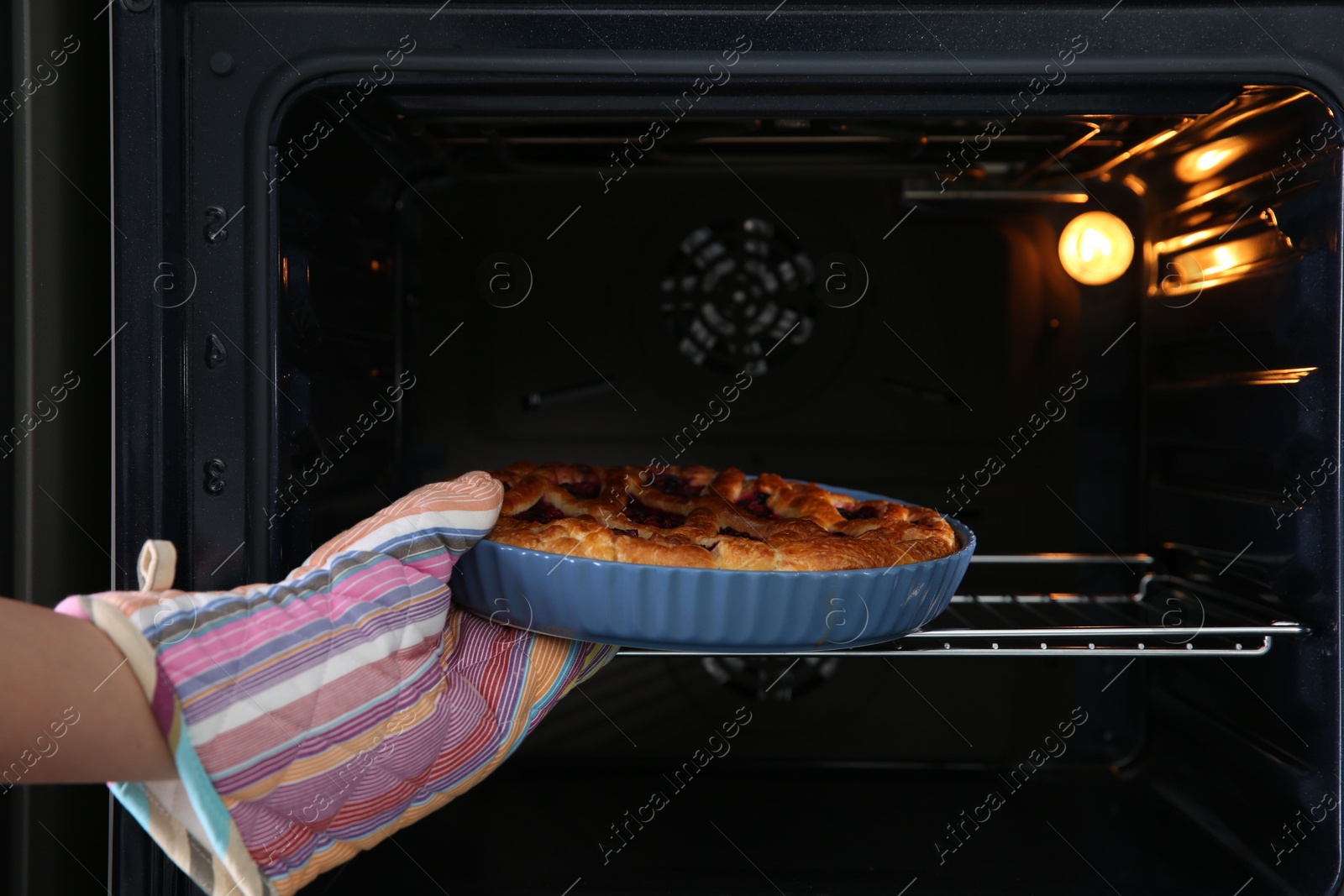 Photo of Woman taking delicious currant pie out of oven, closeup