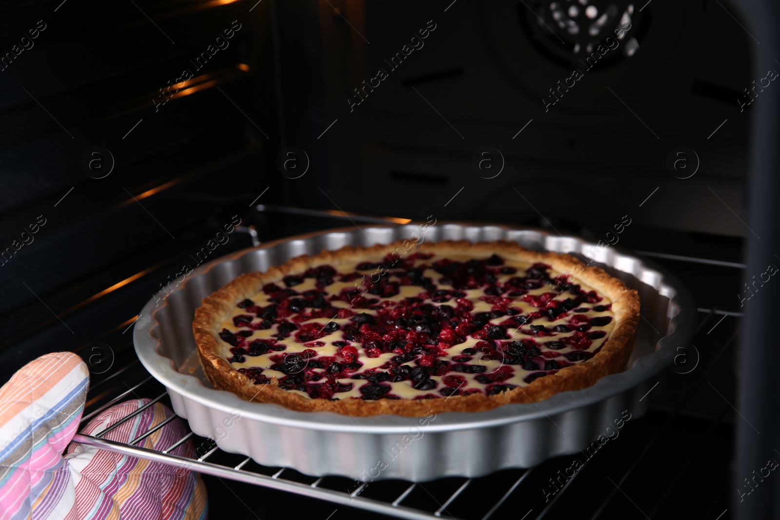 Photo of Woman taking delicious currant pie out of oven, closeup