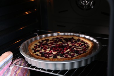 Photo of Woman taking delicious currant pie out of oven, closeup