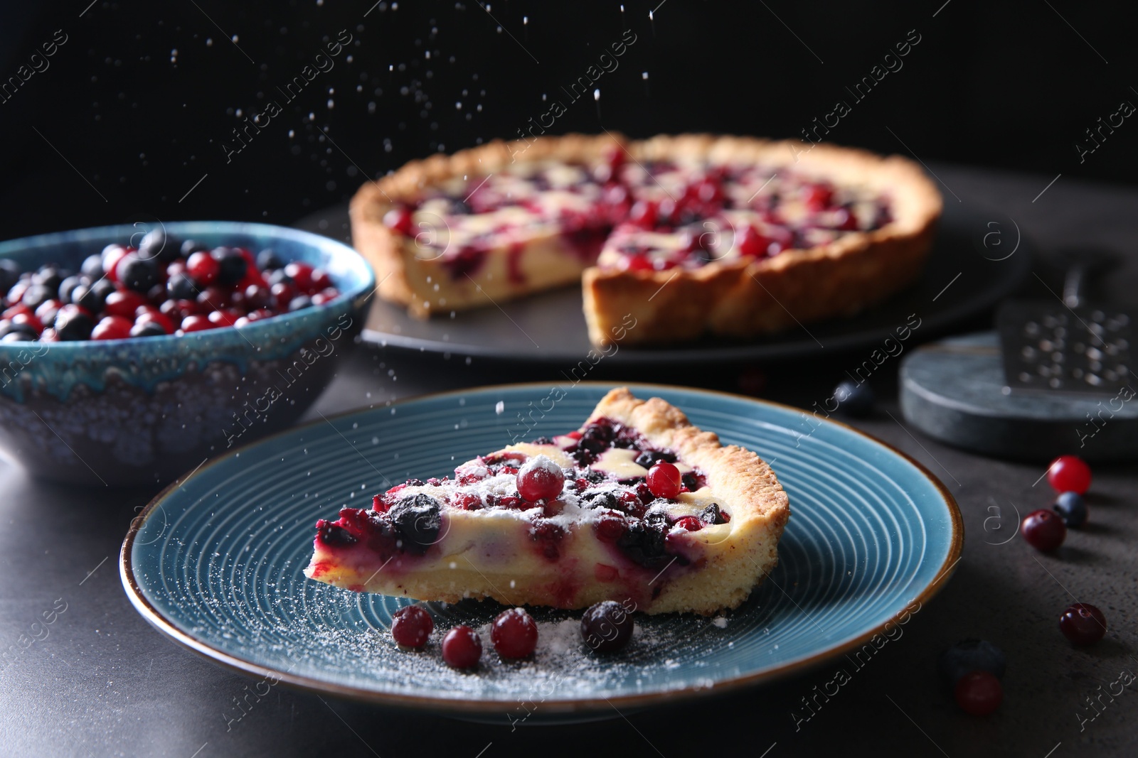 Photo of Sprinkling powdered sugar onto piece of delicious currant pie on grey table, closeup