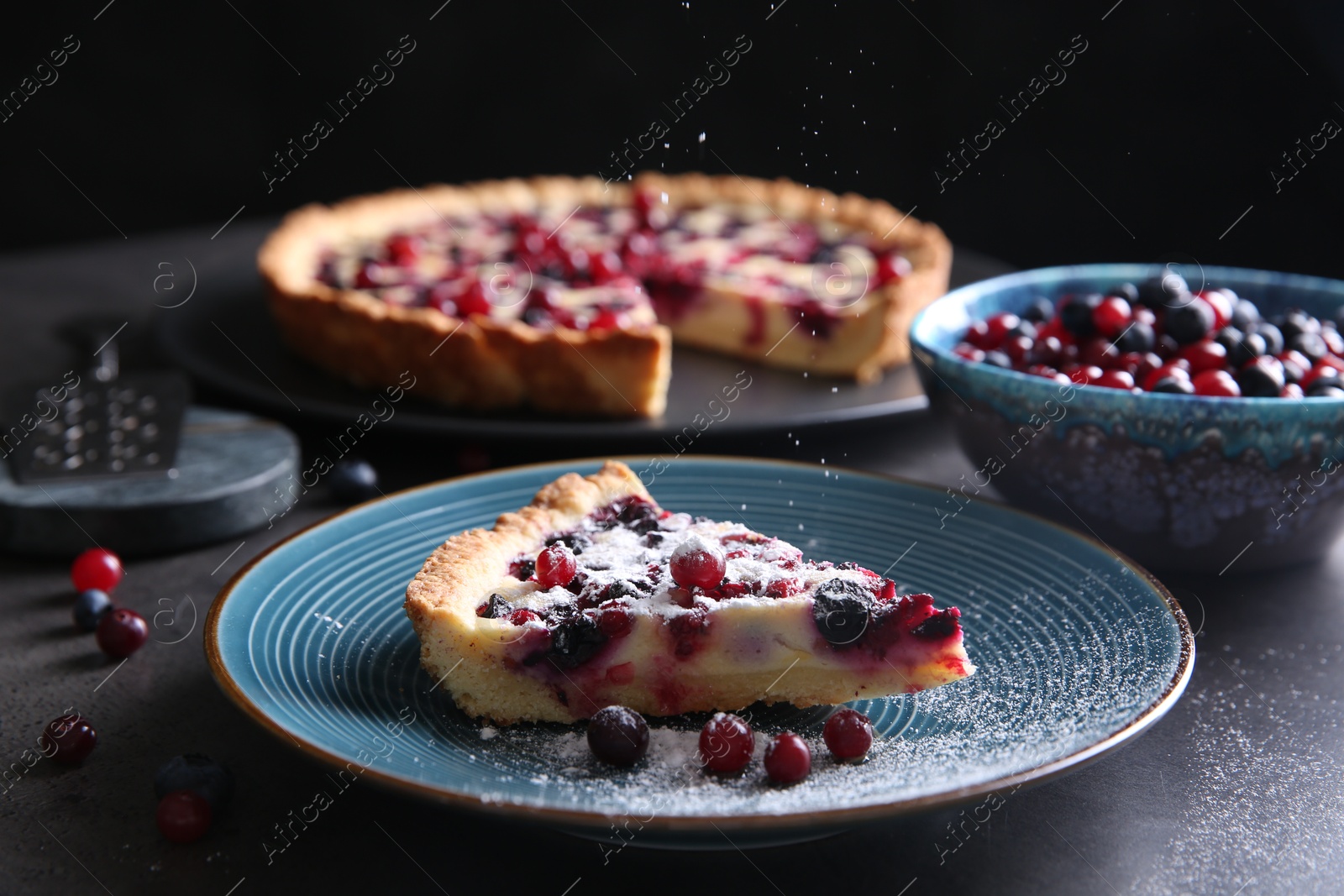 Photo of Sprinkling powdered sugar onto piece of delicious currant pie on grey table, closeup