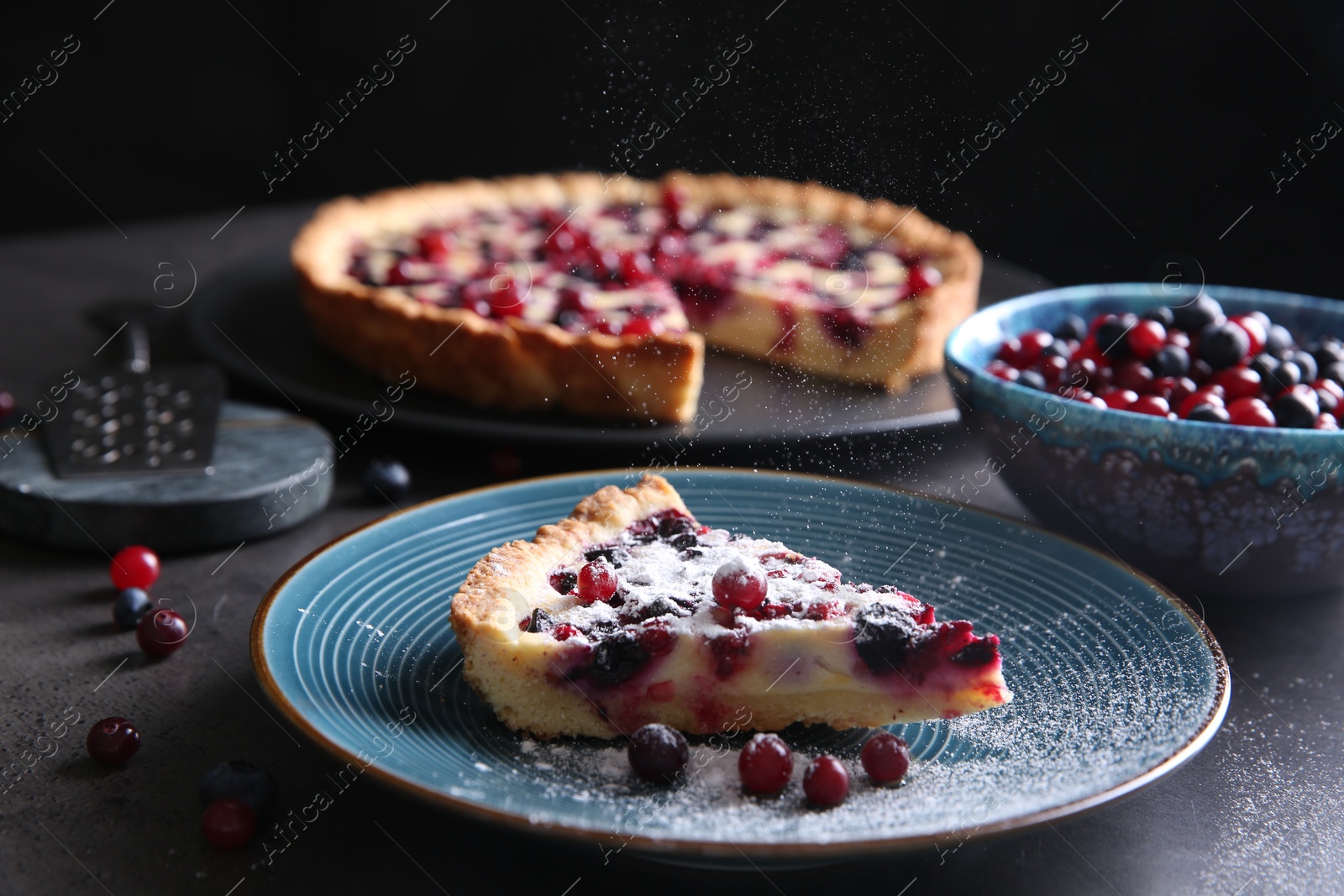 Photo of Sprinkling powdered sugar onto piece of delicious currant pie on grey table, closeup