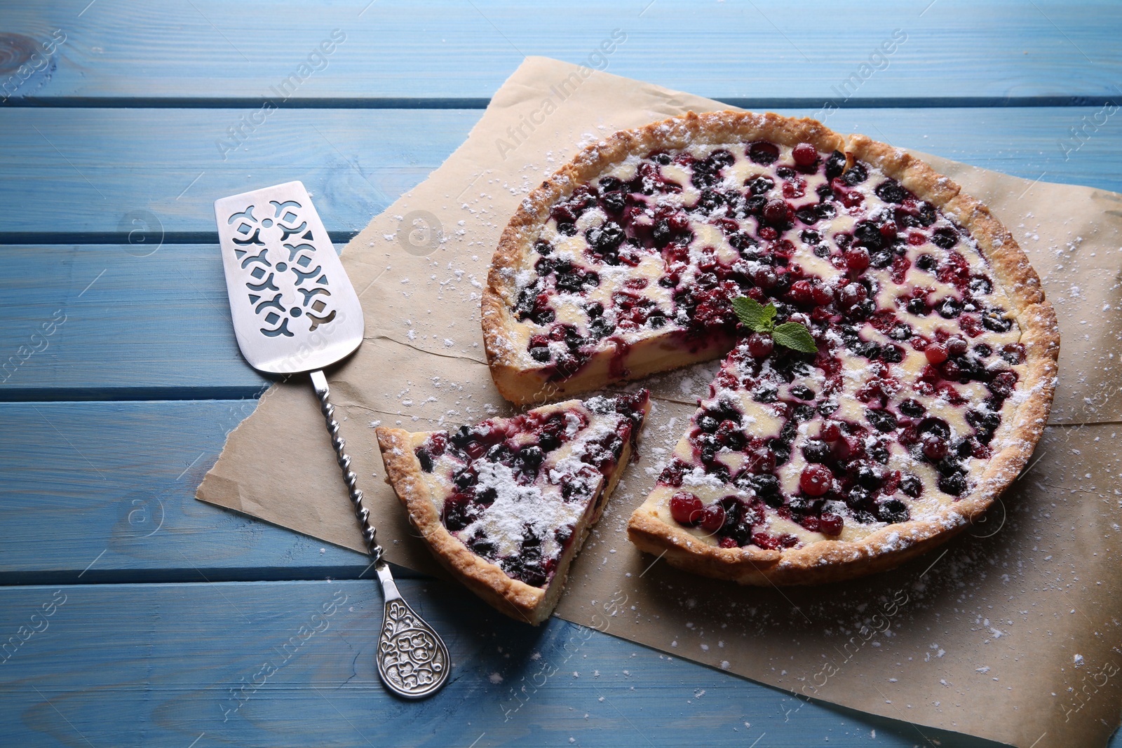 Photo of Delicious cut currant pie and spatula on blue wooden table