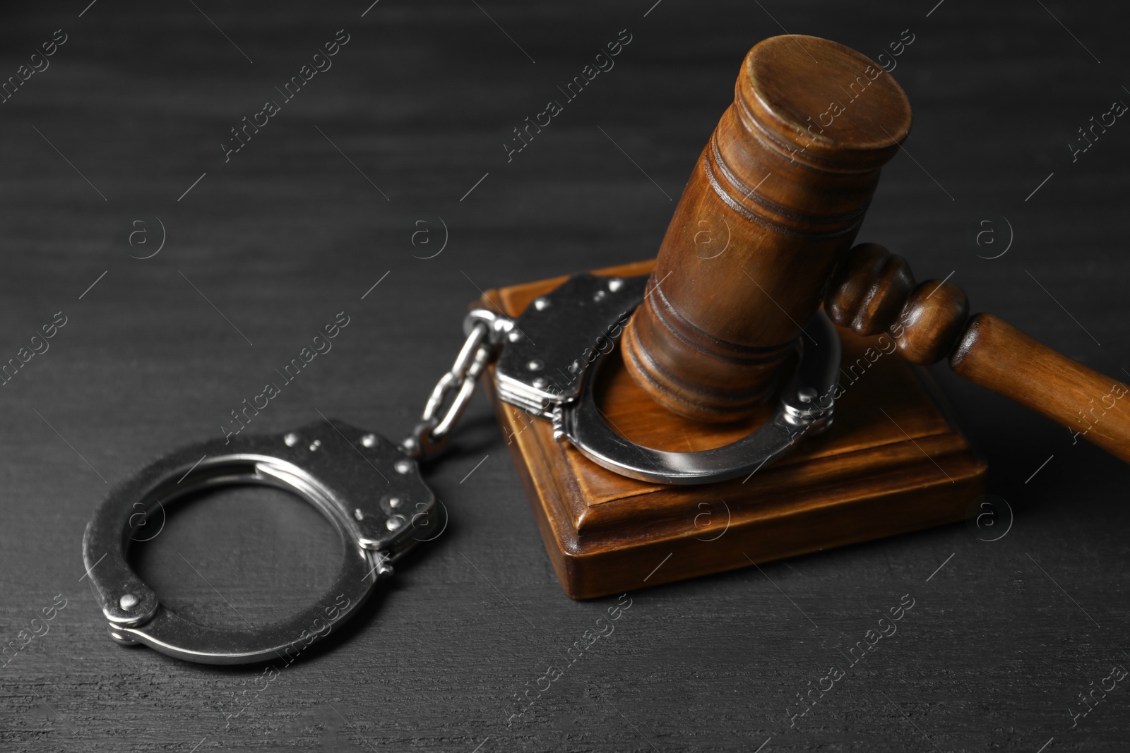 Photo of Handcuffs and judge's gavel on black wooden table, closeup