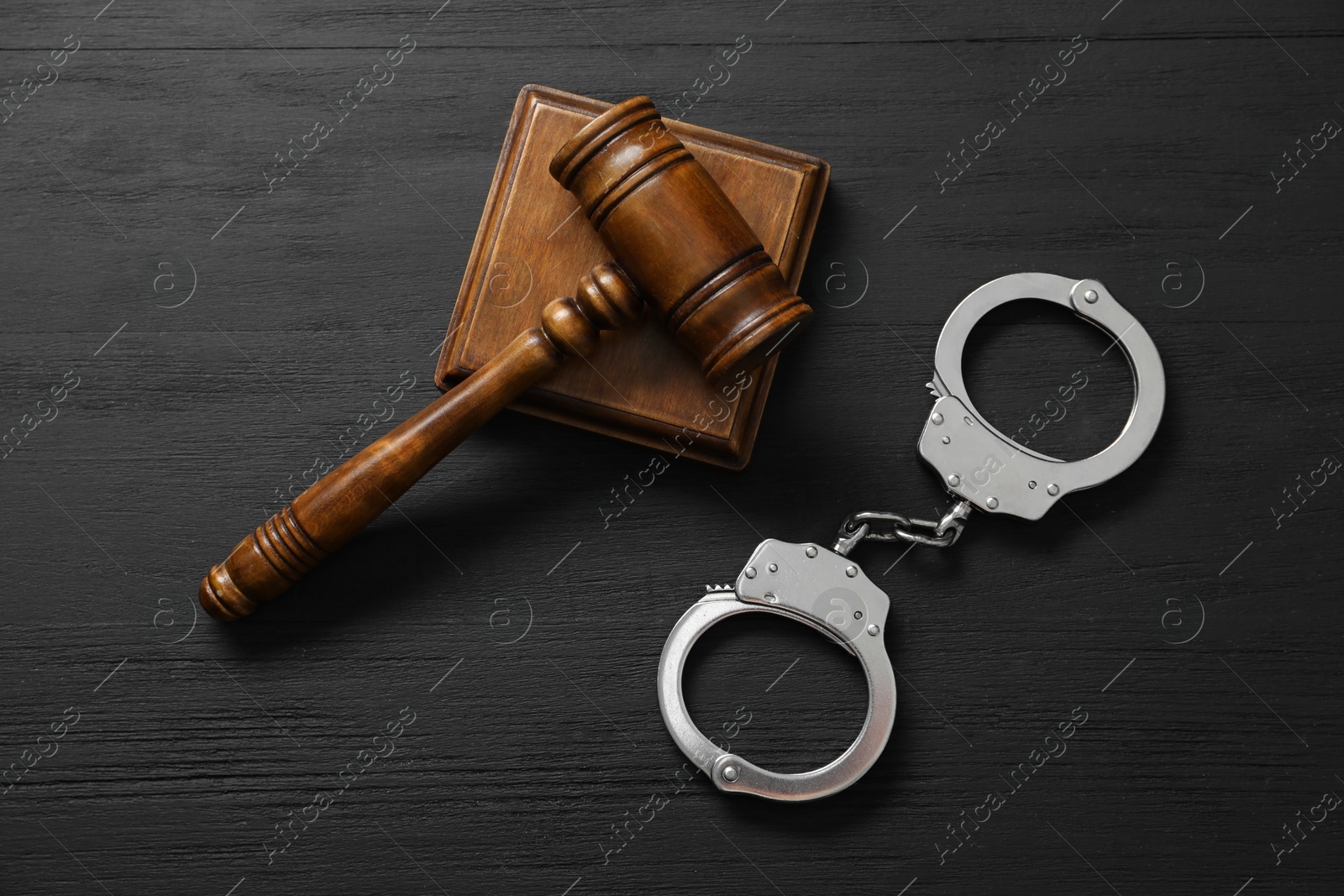 Photo of Handcuffs and judge's gavel on black wooden table, flat lay