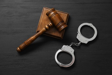 Photo of Handcuffs and judge's gavel on black wooden table, flat lay