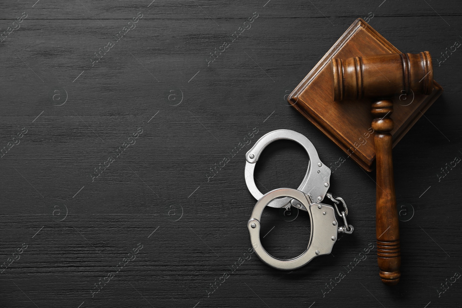 Photo of Handcuffs and judge's gavel on black wooden table, flat lay. Space for text