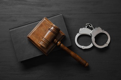 Photo of Handcuffs, book and judge's gavel on black wooden table, flat lay