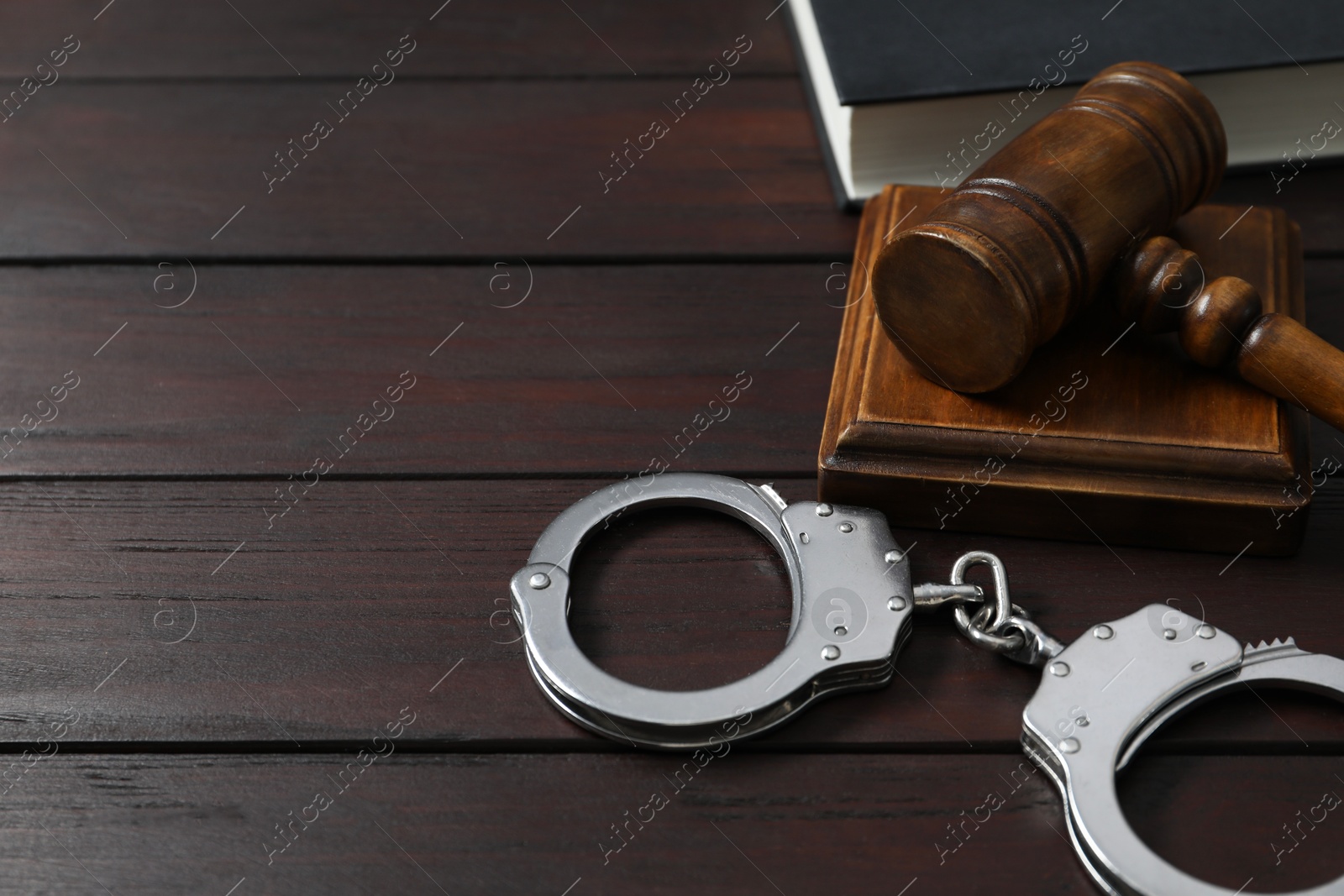 Photo of Handcuffs, judge's gavel and book on wooden table, space for text