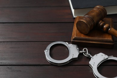 Photo of Handcuffs, judge's gavel and book on wooden table, space for text