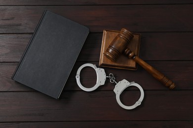 Photo of Handcuffs, judge's gavel and book on wooden table, flat lay