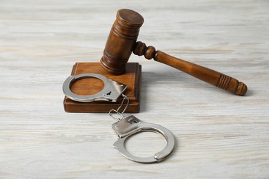 Photo of Handcuffs and judge's gavel on white wooden table