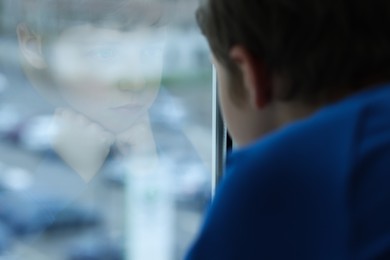 Photo of Autism concept. Lonely little boy near window at home, space for text