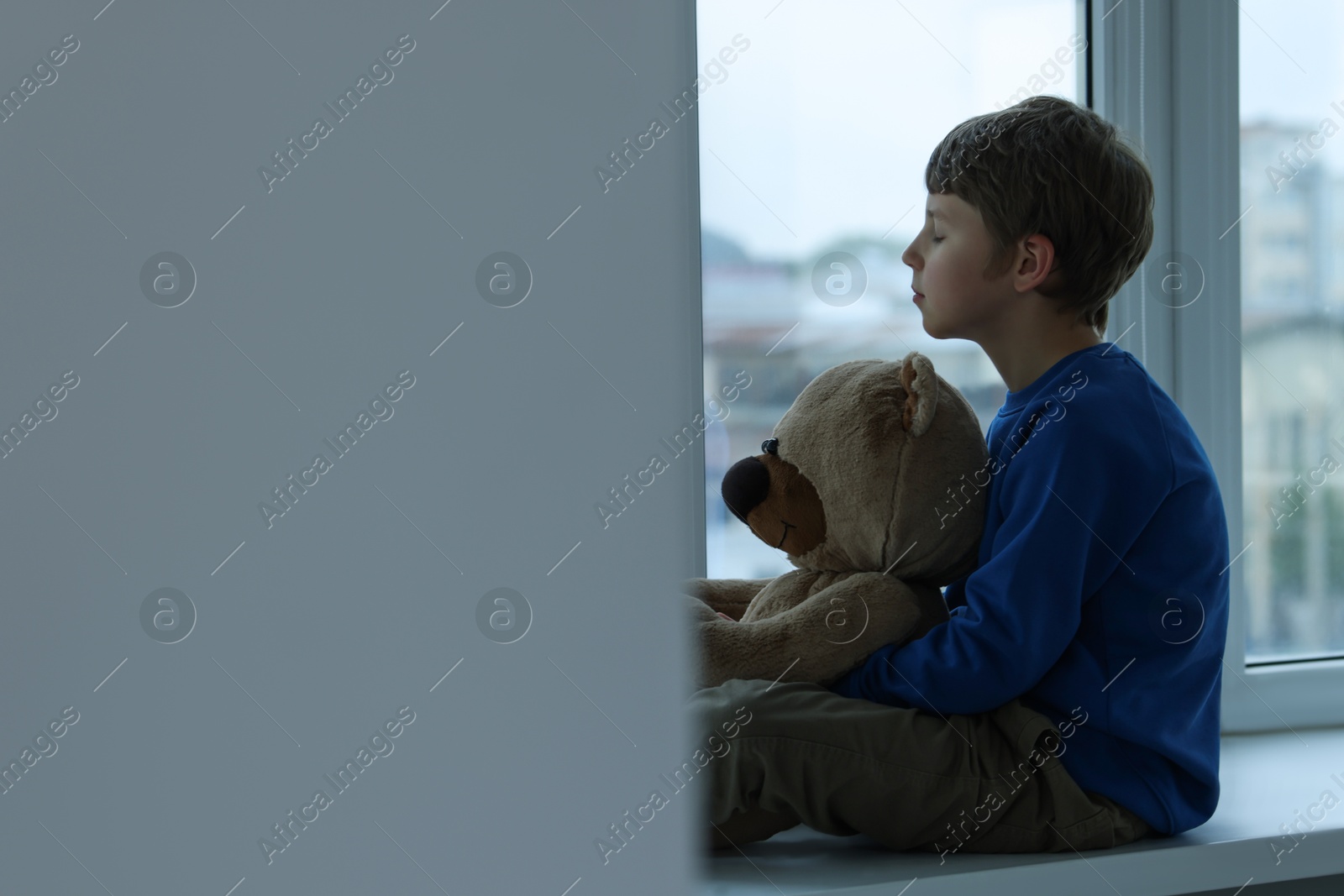 Photo of Autism concept. Lonely little boy with teddy bear near window at home, space for text