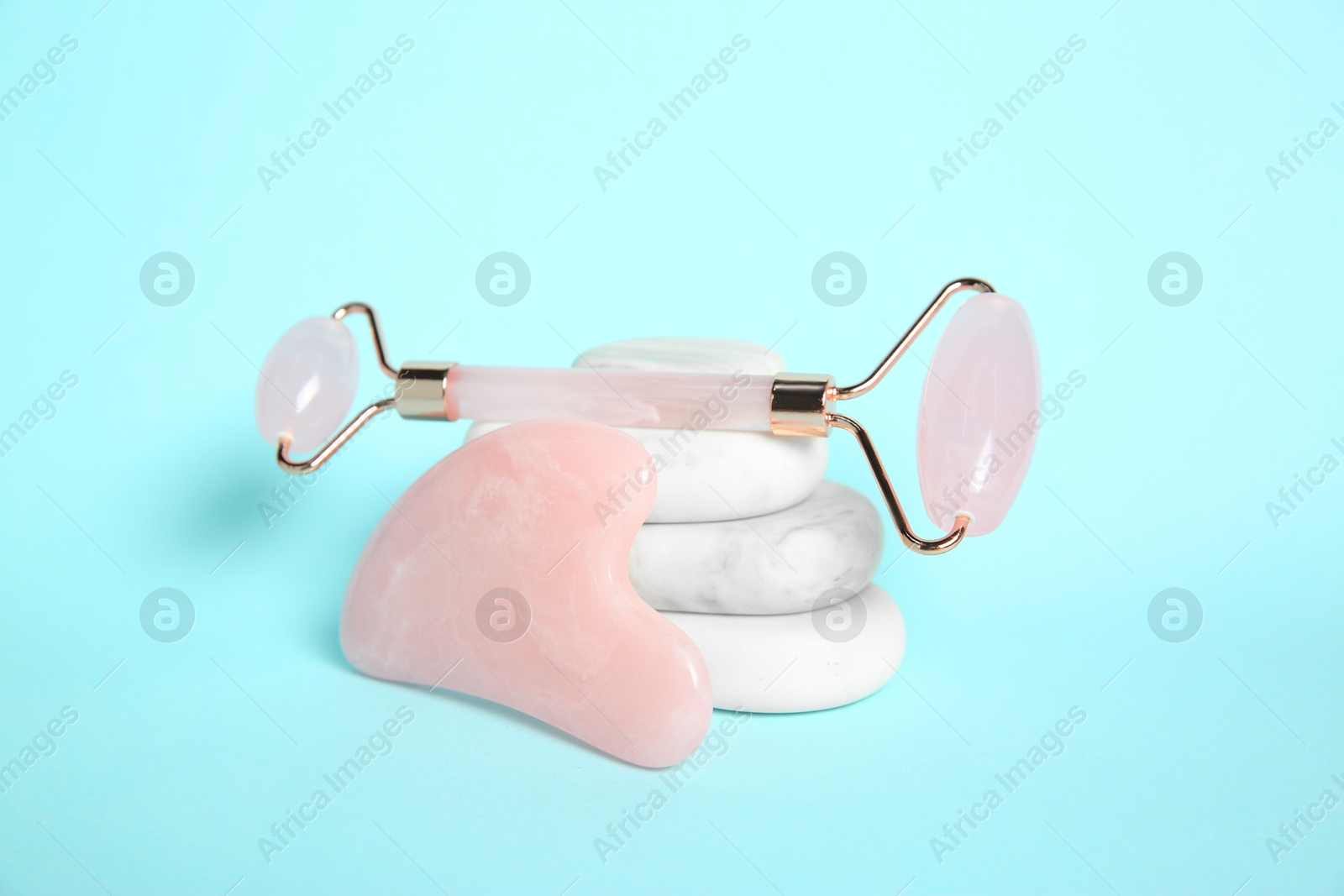 Photo of Rose quartz face roller, gua sha tool and spa stones on light blue background