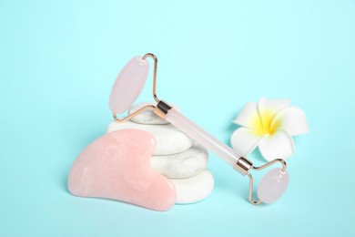 Photo of Rose quartz face roller, gua sha tool, plumeria flower and spa stones on light blue background