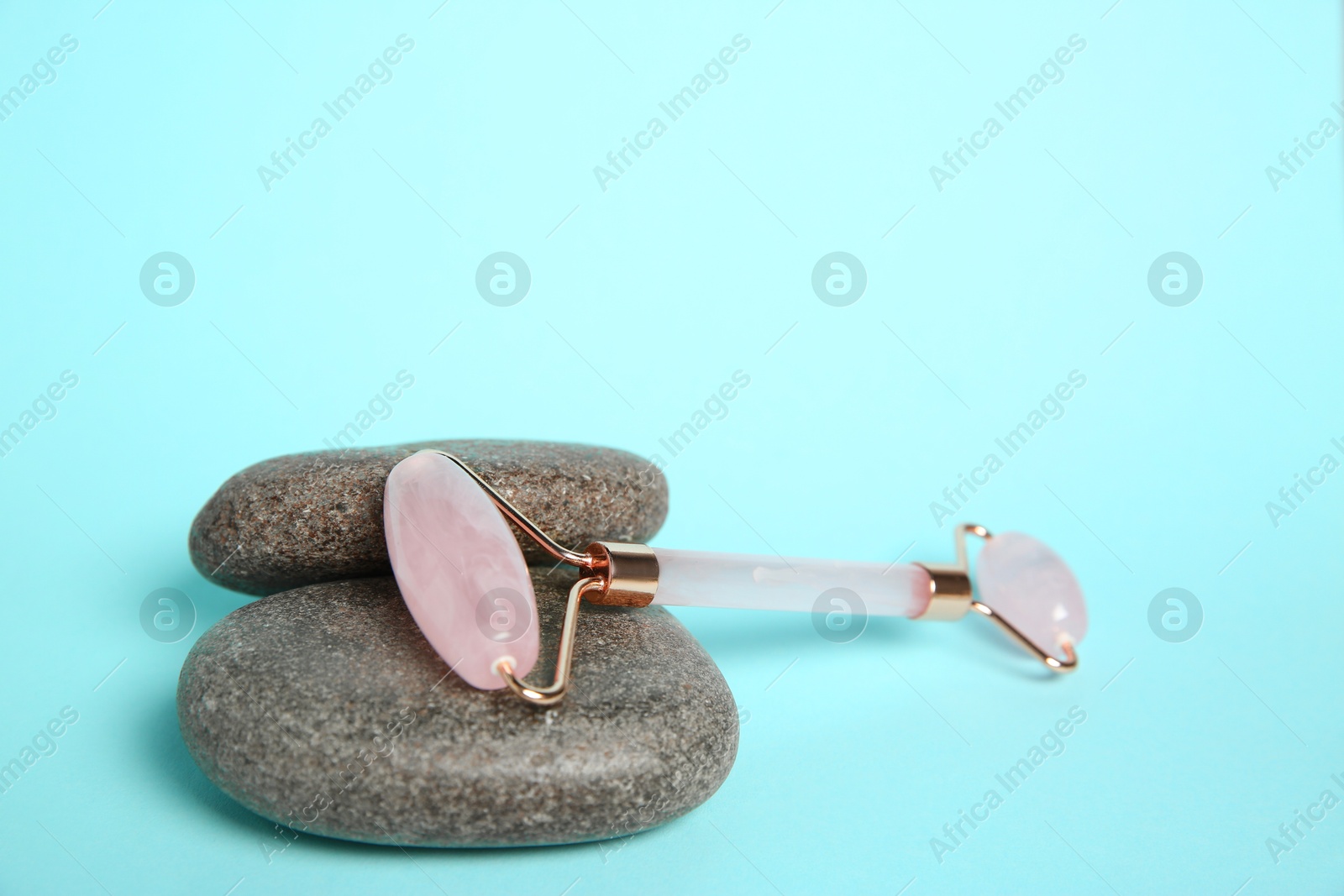 Photo of Rose quartz face roller and stones on light blue background