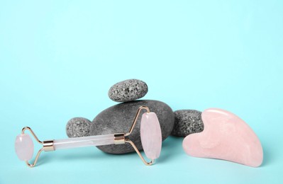 Photo of Rose quartz face roller, gua sha tool and stones on light blue background