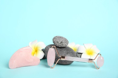 Photo of Rose quartz face roller, gua sha tool, plumeria flowers and stones on light blue background