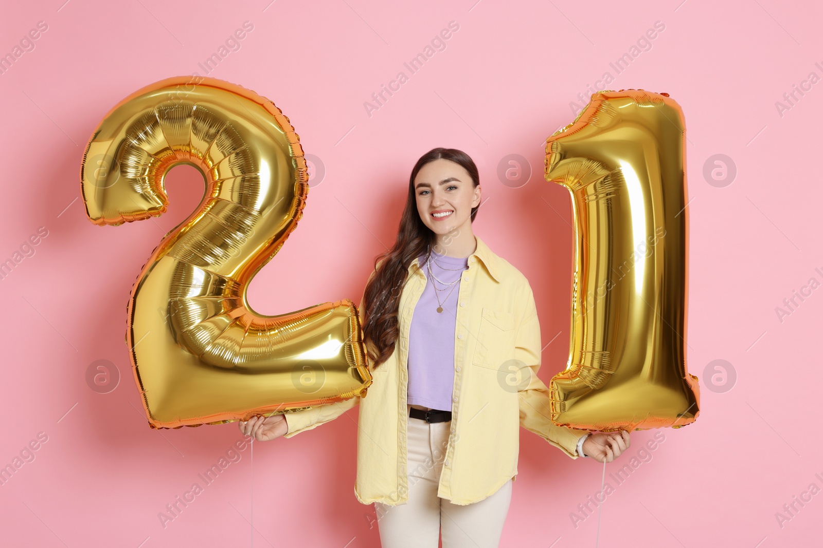 Photo of Coming of age party - 21st birthday. Happy young woman with number shaped balloons on pink background