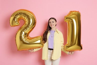 Photo of Coming of age party - 21st birthday. Happy young woman with number shaped balloons on pink background