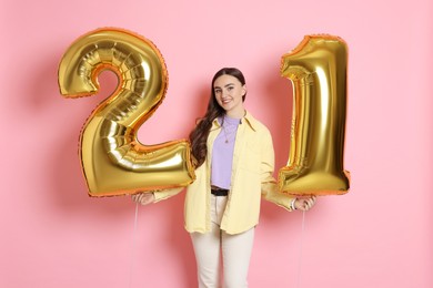 Photo of Coming of age party - 21st birthday. Happy young woman with number shaped balloons on pink background