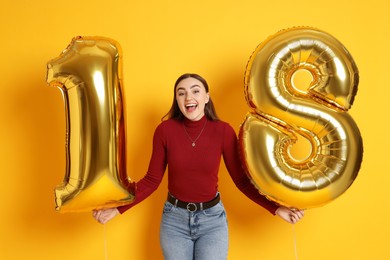 Photo of Coming of age party - 18th birthday. Happy young woman with number shaped balloons on yellow background