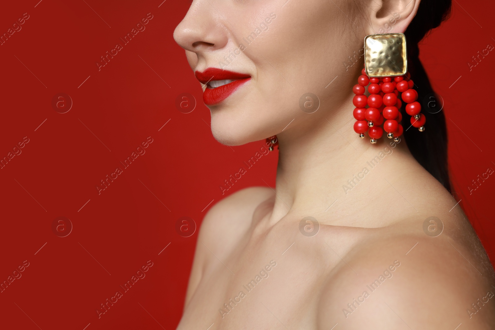 Photo of Beautiful young woman wearing elegant earrings on red background, closeup. Space for text