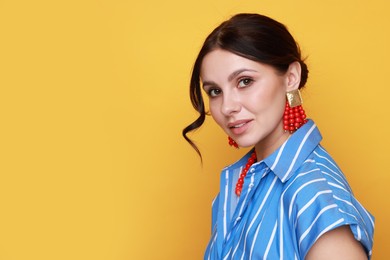 Photo of Young woman wearing stylish earrings and necklace on orange background. Space for text