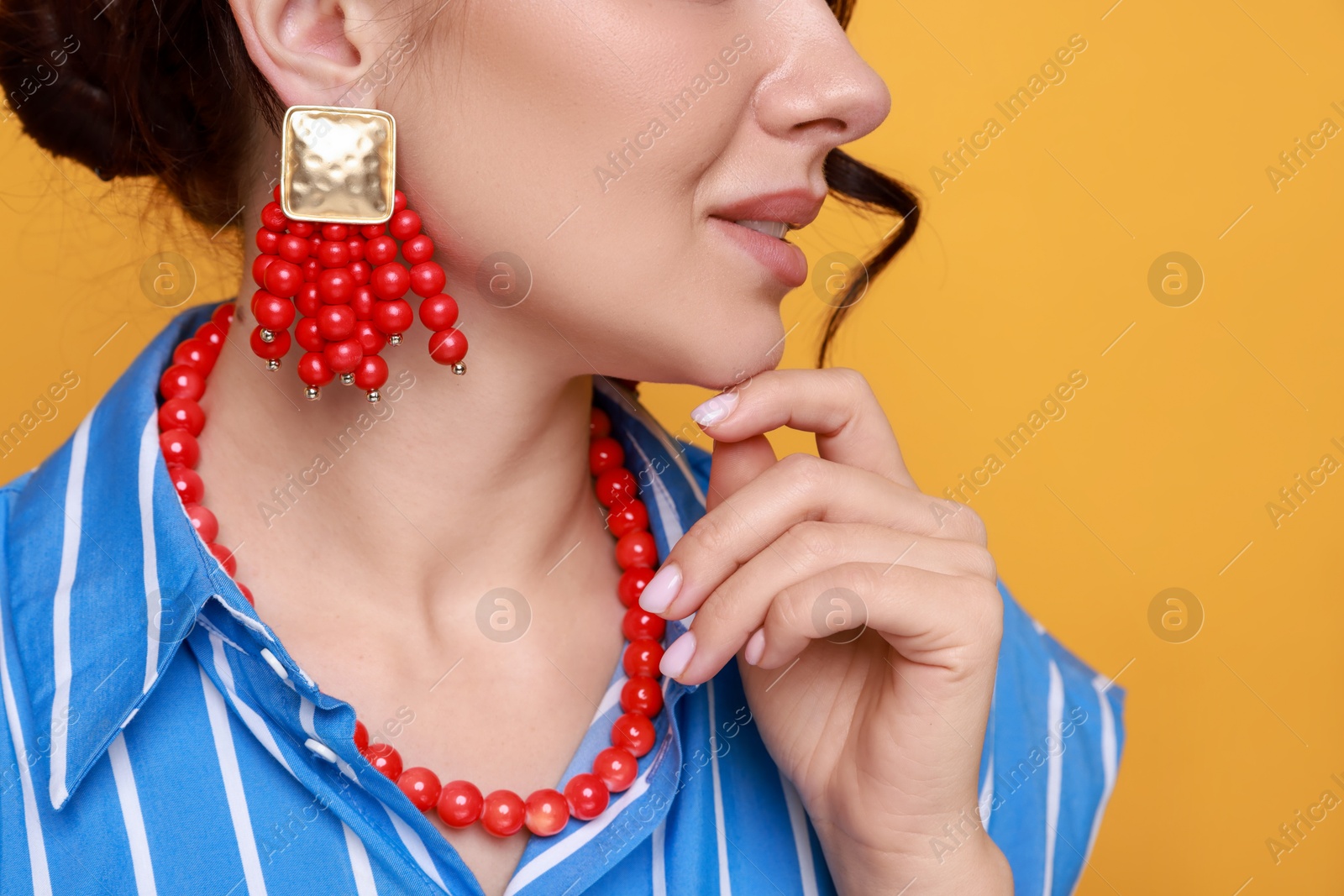 Photo of Young woman wearing stylish earrings and necklace on orange background, closeup