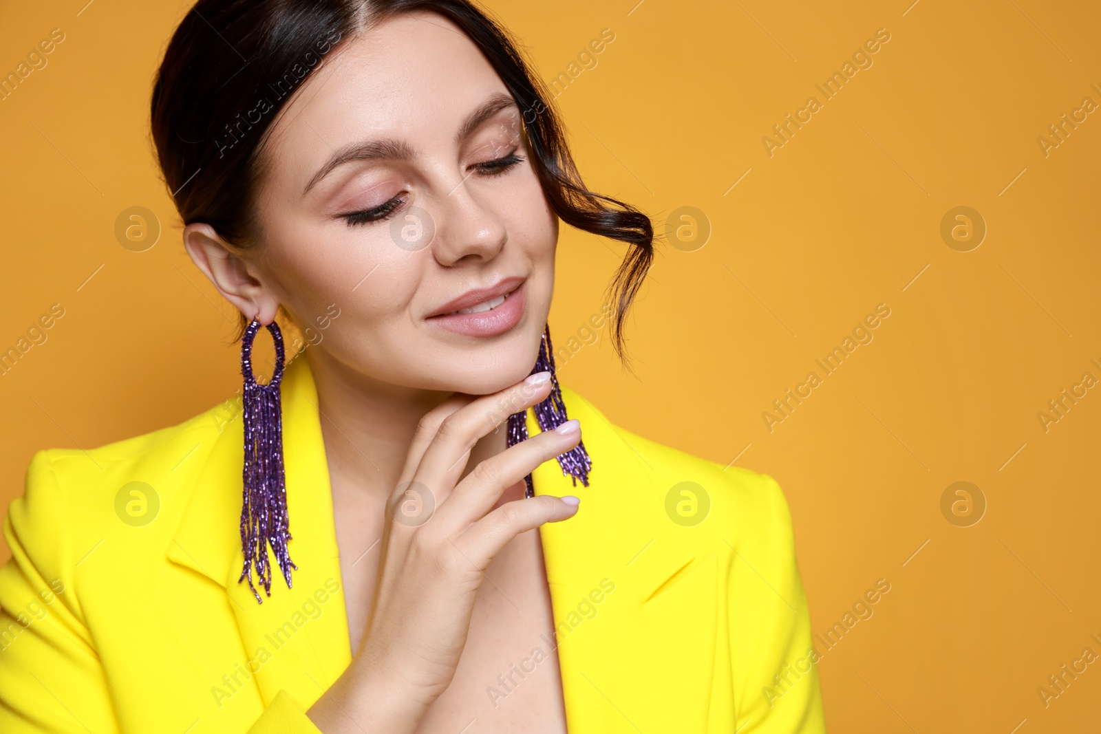 Photo of Beautiful young woman wearing stylish earrings on orange background. Space for text