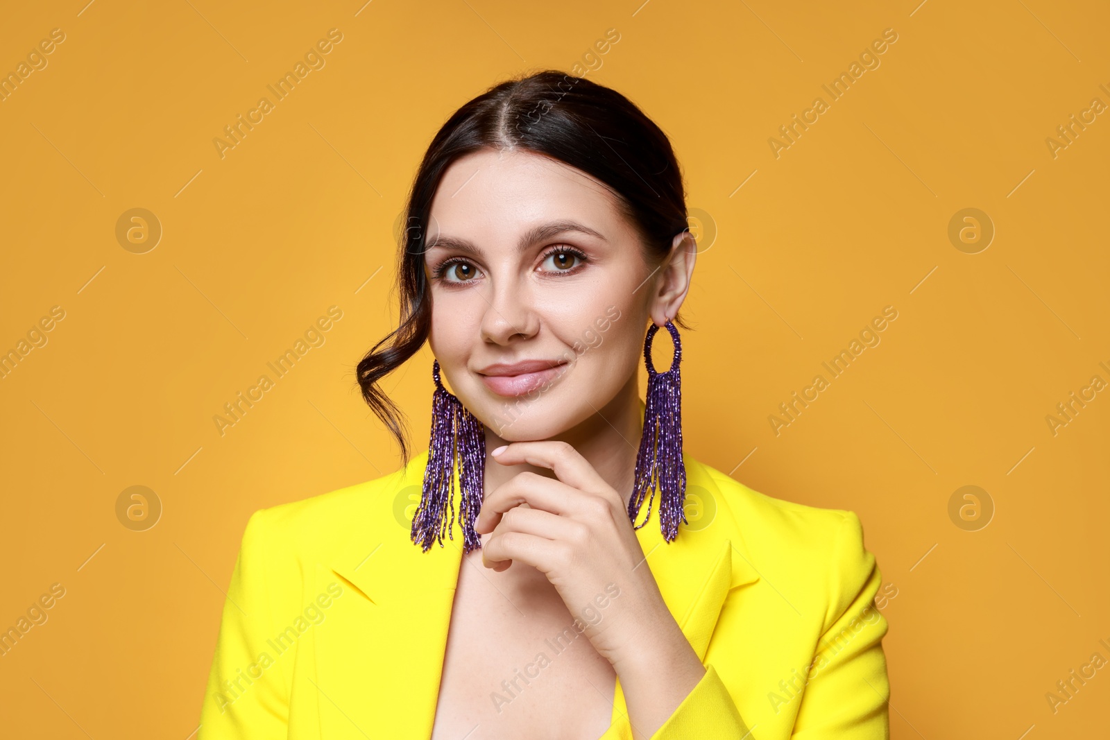 Photo of Beautiful young woman wearing stylish earrings on orange background