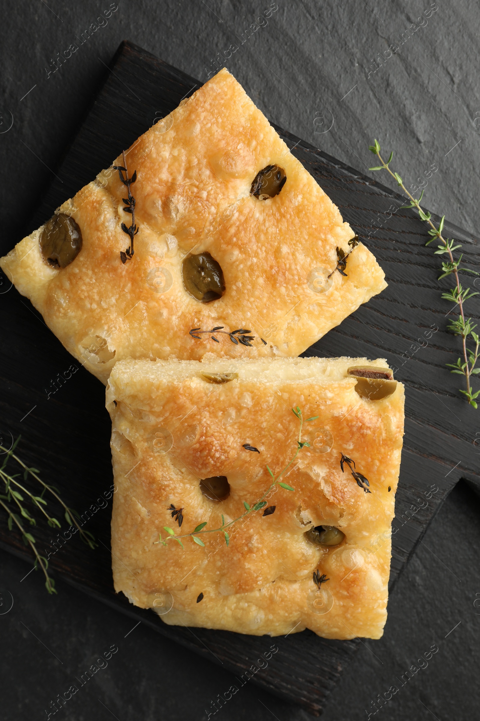 Photo of Pieces of delicious focaccia bread with olives and thyme on black table, flat lay