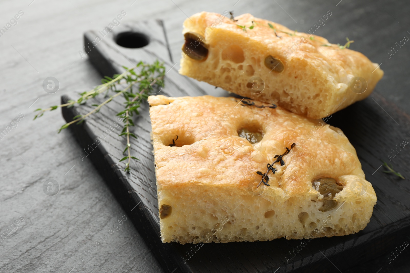 Photo of Pieces of delicious focaccia bread with olives and thyme on black table, closeup