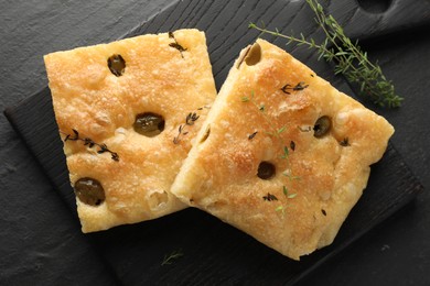 Photo of Pieces of delicious focaccia bread with olives and thyme on black table, flat lay