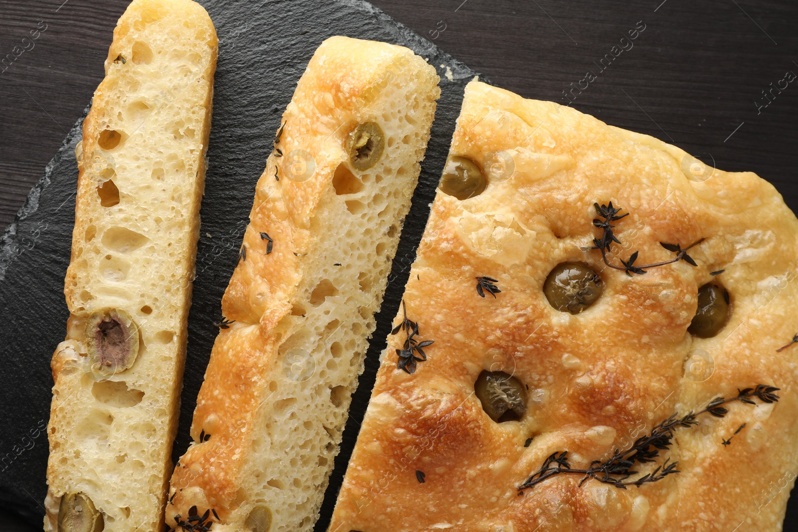 Photo of Pieces of delicious focaccia bread with olives and thyme on dark wooden table, top view