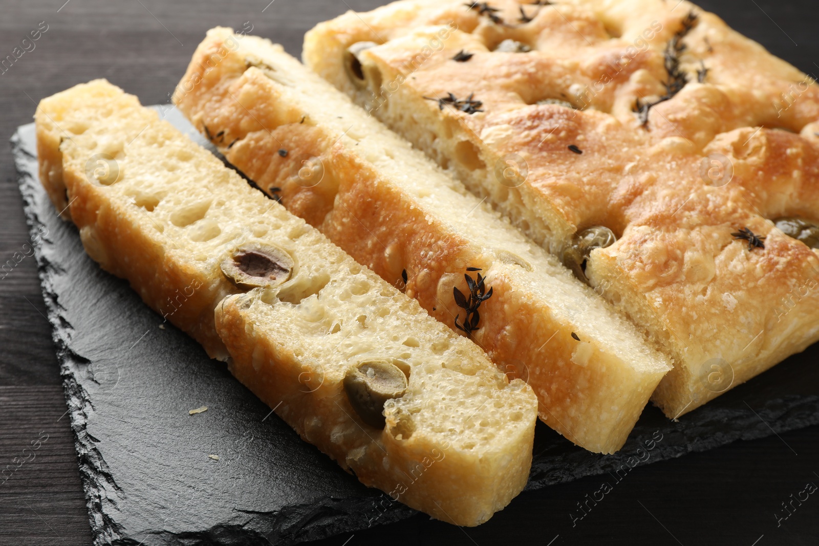 Photo of Pieces of delicious focaccia bread with olives and thyme on dark wooden table, closeup