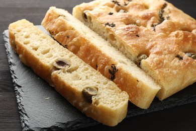 Photo of Pieces of delicious focaccia bread with olives and thyme on dark wooden table, closeup