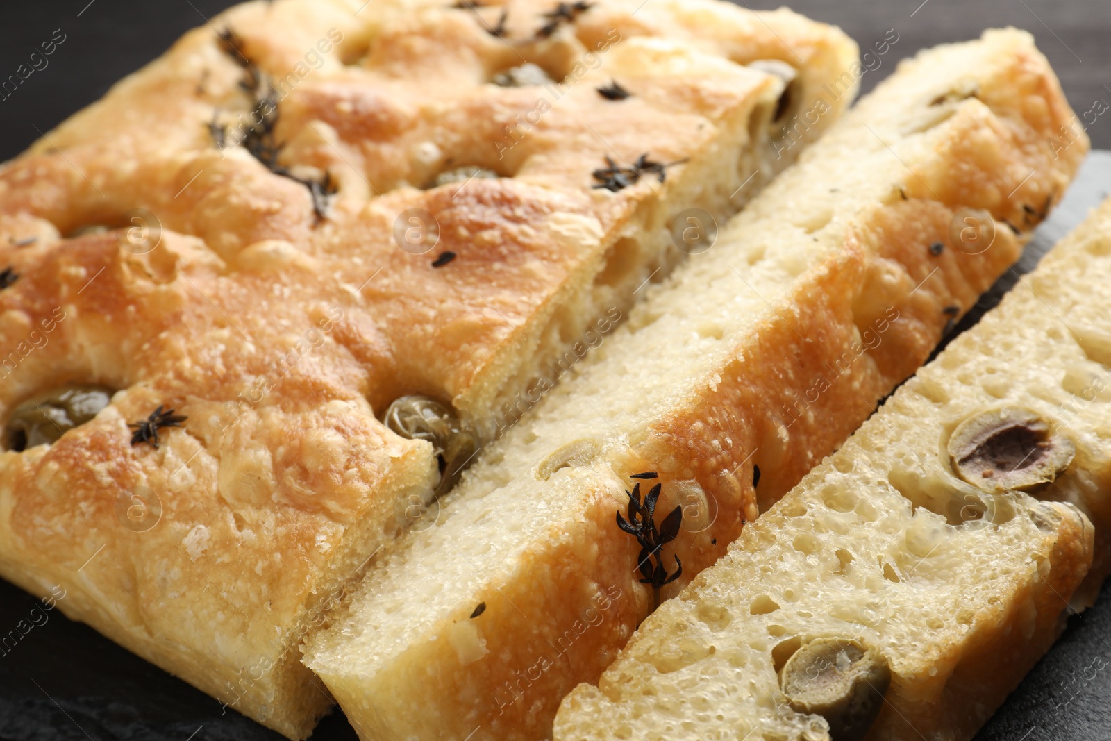 Photo of Pieces of delicious focaccia bread with olives and thyme on table, closeup