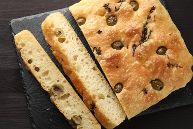 Photo of Pieces of delicious focaccia bread with olives and thyme on dark wooden table, top view