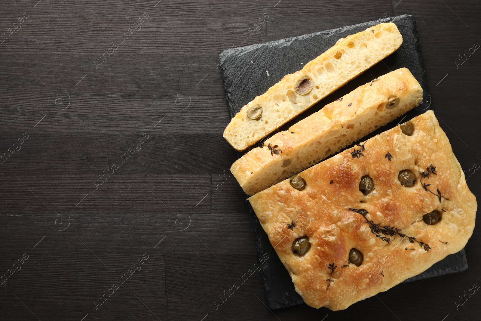 Photo of Pieces of delicious focaccia bread with olives and thyme on dark wooden table, top view. Space for text