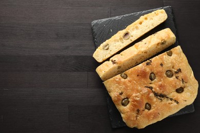 Photo of Pieces of delicious focaccia bread with olives and thyme on dark wooden table, top view. Space for text